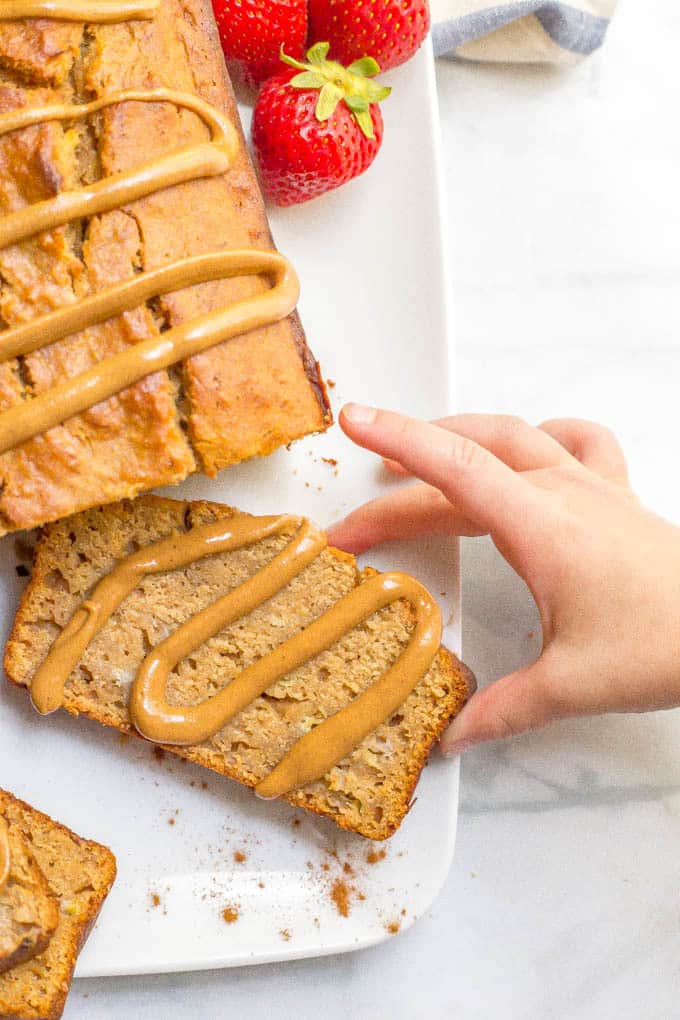 Whole wheat peanut butter banana bread with hand reaching from the side for a slice