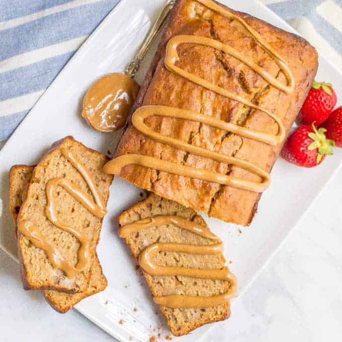 Peanut butter banana bread served on a white platter with a few slices cut and a drizzle of peanut butter over the whole thing.