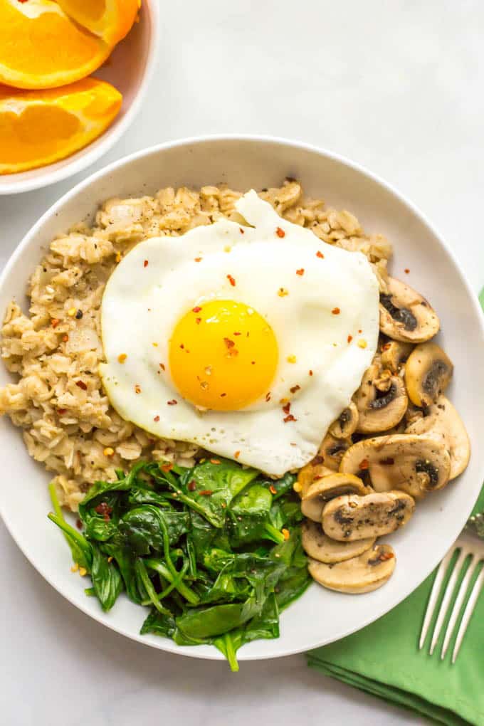 Savory oatmeal bowl with sauteed mushrooms, spinach and a fried egg on top in a bowl with oranges on side