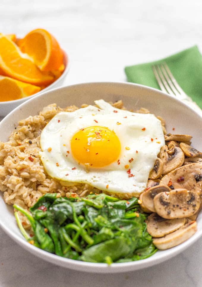 Savory oatmeal bowl with sauteed mushrooms, spinach and a fried egg on top in a bowl with red pepper flakes on top