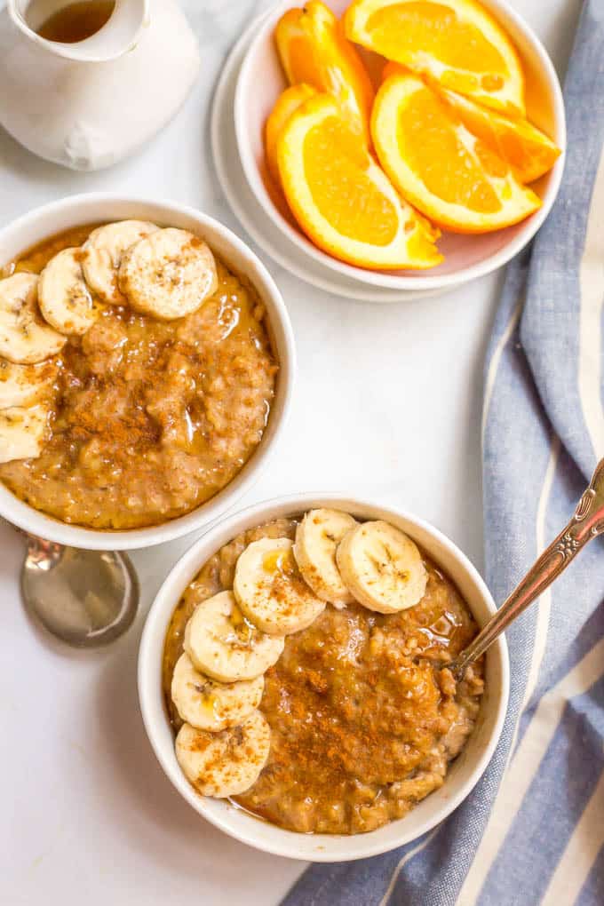 Slow cooker maple cinnamon oatmeal in bowls with sliced bananas and a side of oranges