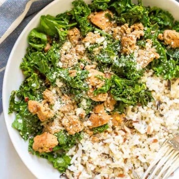 Close up of a bowl with wild rice alongside a turkey sausage and kale mixture, all topped with Parmesan cheese.