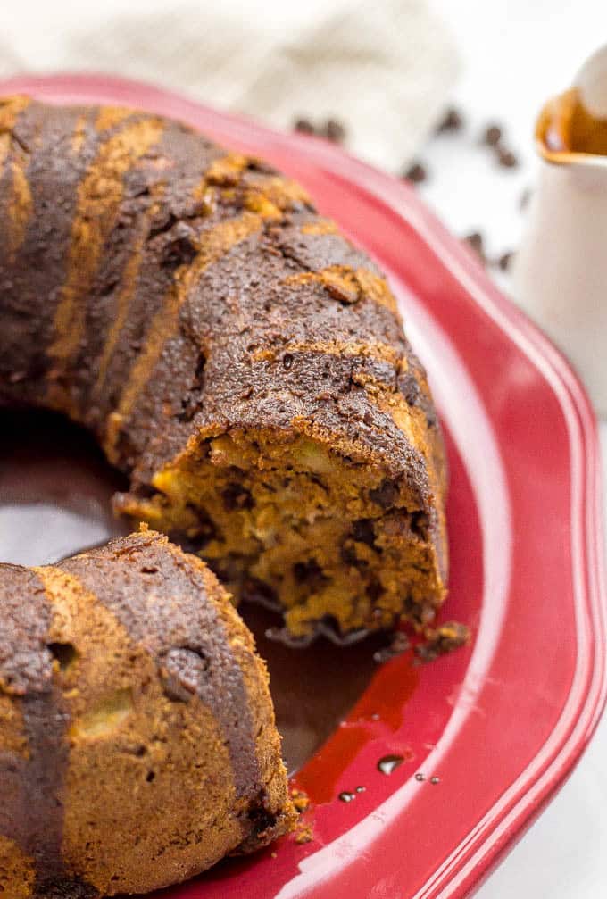 Close up of a sliced section of a chocolate chip apple cake with chocolate sauce on top on a red platter.