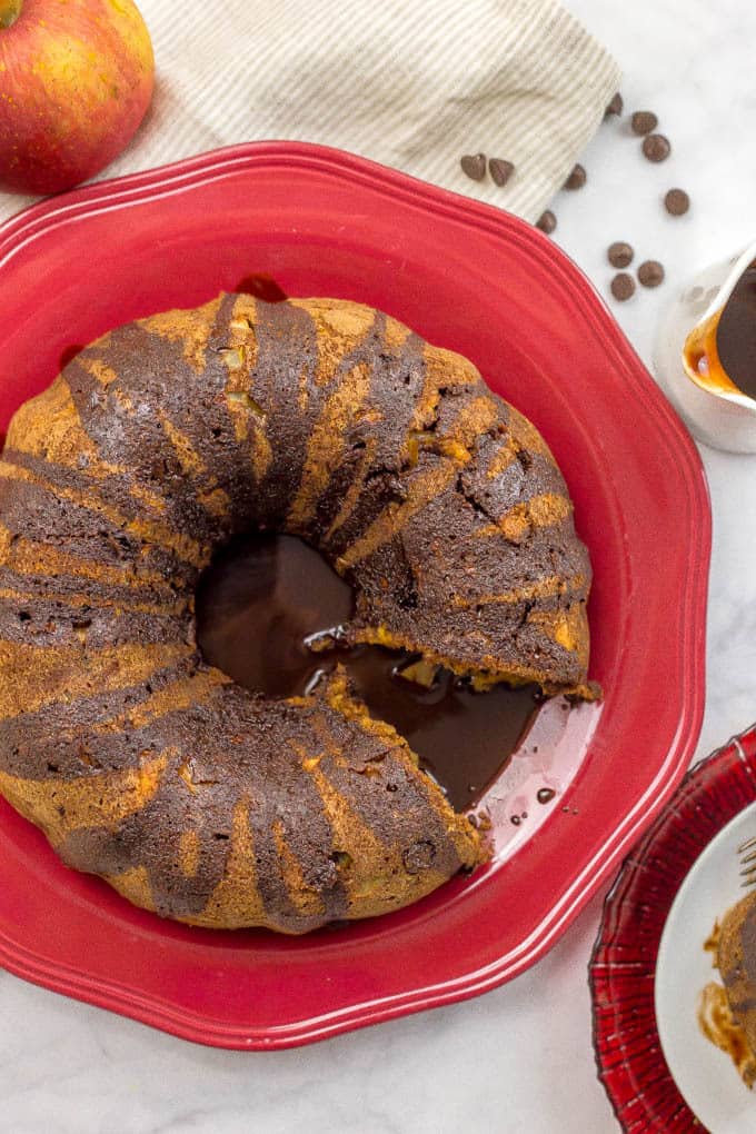 An apple chocolate chip cake on a red platter with a slice removed and served on a plate to the side.
