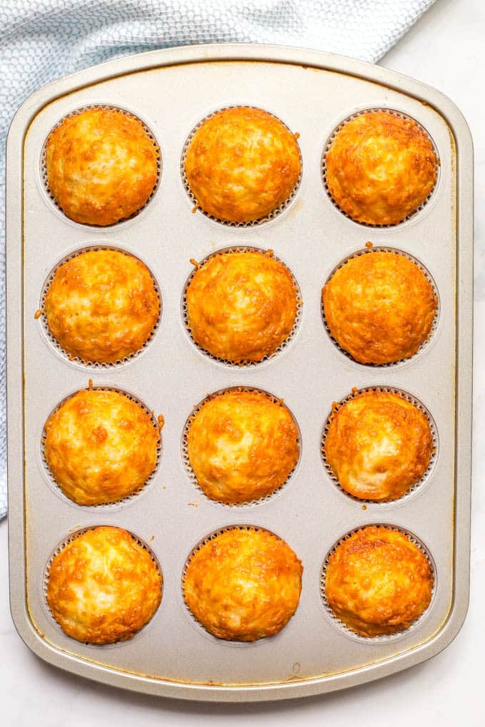 A 12 cup muffin tin full of baked, golden brown cheesy cornbread muffins.