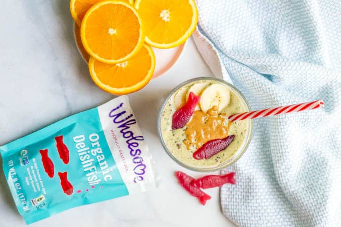 Peanut butter banana smoothie in a glass cup with Wholesome candy fish and oranges