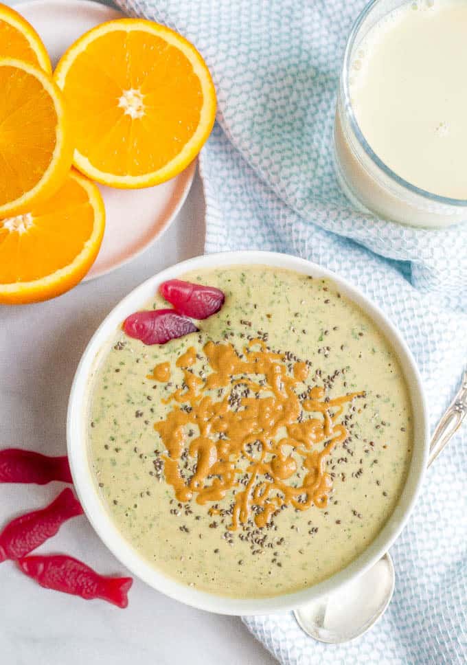 Peanut butter banana smoothie bowl with organic fish candies, glass of milk and cut oranges