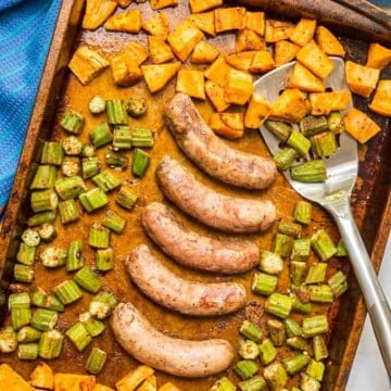 A sheet pan with roasted sweet potatoes and okra and browned links of turkey sausage in the middle.
