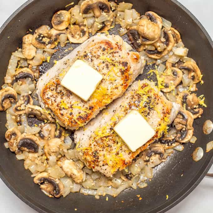 Overhead angle of Garlic butter pork chops with butter and lemon zest, in pan surrounded by onions and mushrooms