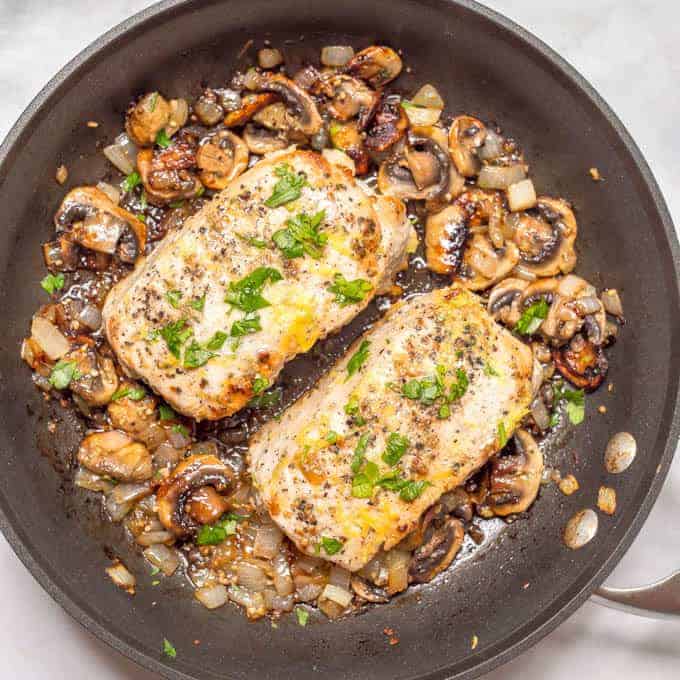 Overhead angle of garlic butter pork chops with parsley and lemon zest, in pan surrounded by onions and mushrooms