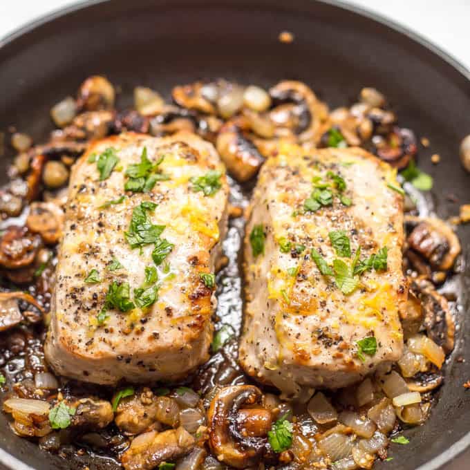 Garlic butter pork chops with parsley and lemon zest, in pan surrounded by onions and mushrooms