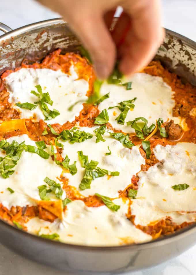 Easy healthy one pot lasagna in pan after baking with melted mozzarella cheese on top and fresh basil being sprinkled on