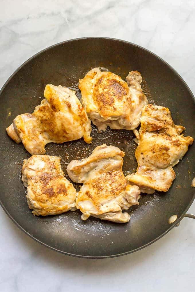 Chicken thighs being seared in a pan