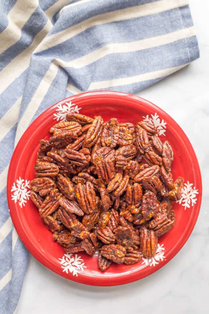Pecans with a sweet and spicy glaze served on a red holiday plate.