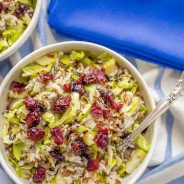 A fork resting in a white bowl filled with a wild rice and shredded Brussels sprout salad topped with dried cranberries.
