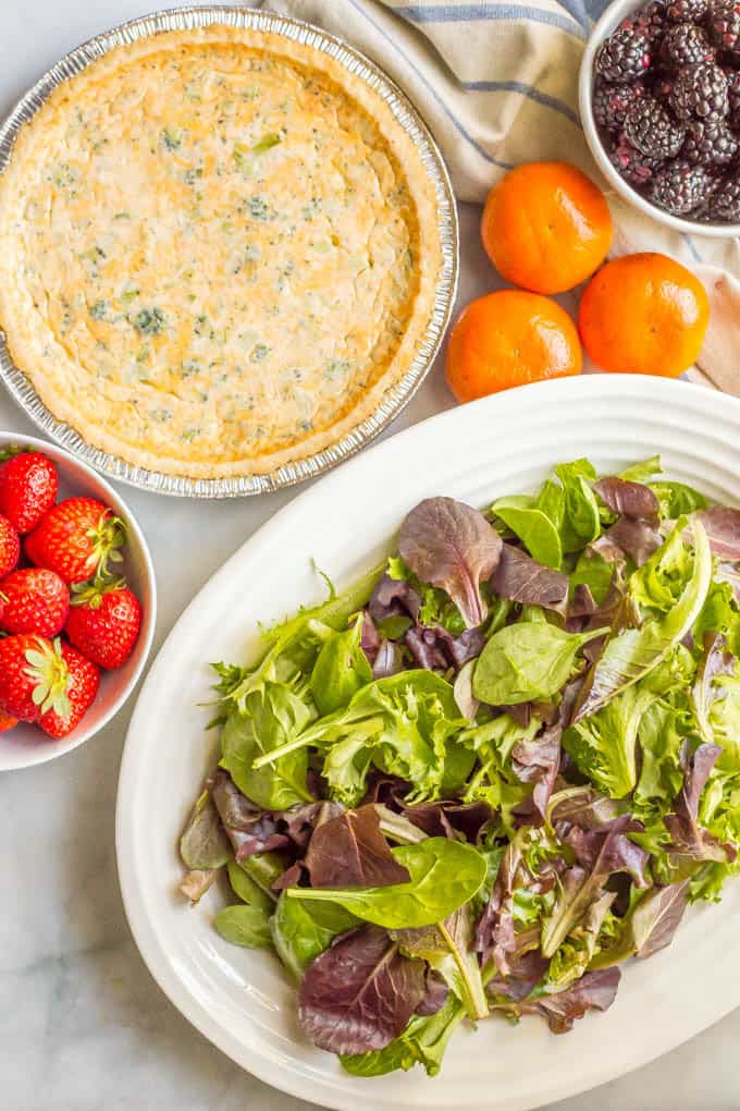 Mixed greens salad with fruit ingredients arranged with a quiche