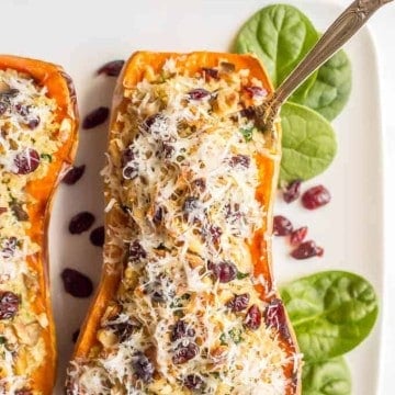 A fork resting in a stuffed butternut squash half loaded with quinoa, mushrooms, spinach and dried cranberries with grated Parmesan on top.