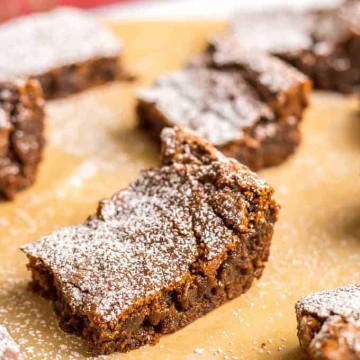 Close up of a gingerbread cookie bar with powdered sugar on top resting on a piece of parchment paper.