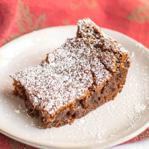 A single whole wheat gingerbread bar with powdered sugar on a white plate