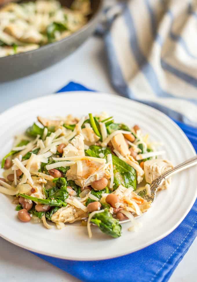 White plate of chicken with beans, spinach and cheese served with a fork