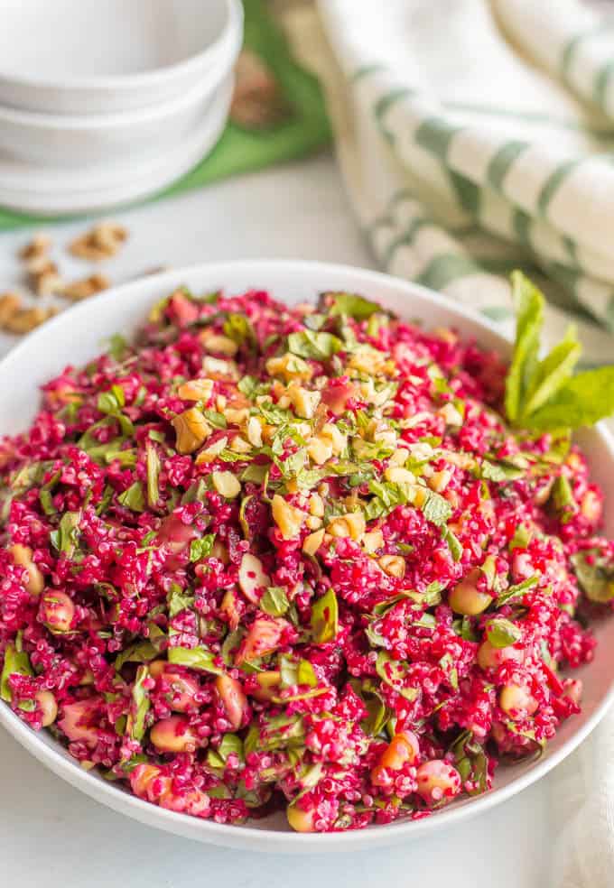 A chopped beet and quinoa salad with spinach, edamame and walnuts served in a white bowl with a sprig of fresh mint on the size.