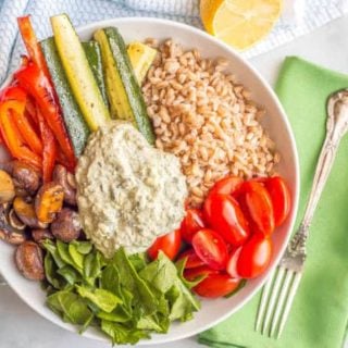 Overhead shot of farro and roasted vegetable grain bowl with spinach and kale dip and a green napkin with a fork on the side