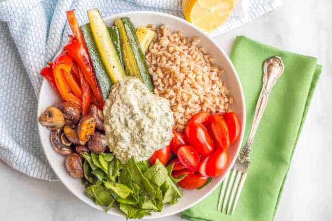 Overhead shot of farro and roasted vegetable grain bowl with spinach and kale dip and a green napkin with a fork on the side