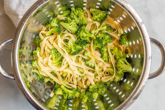 Cooked fettuccine noodles and broccoli in a colander