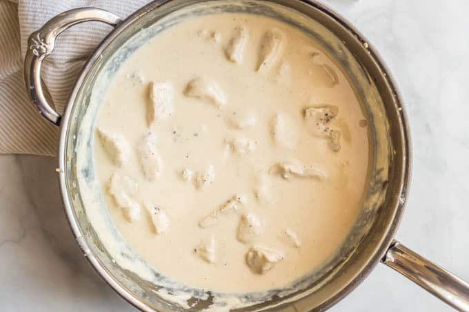 Chicken and healthy Alfredo sauce in a large saute pan on a marble surface