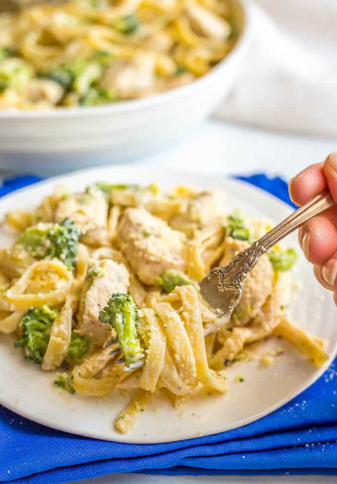 Healthy chicken Alfredo with broccoli on a white plate with blue napkin underneath and a forkful being taken