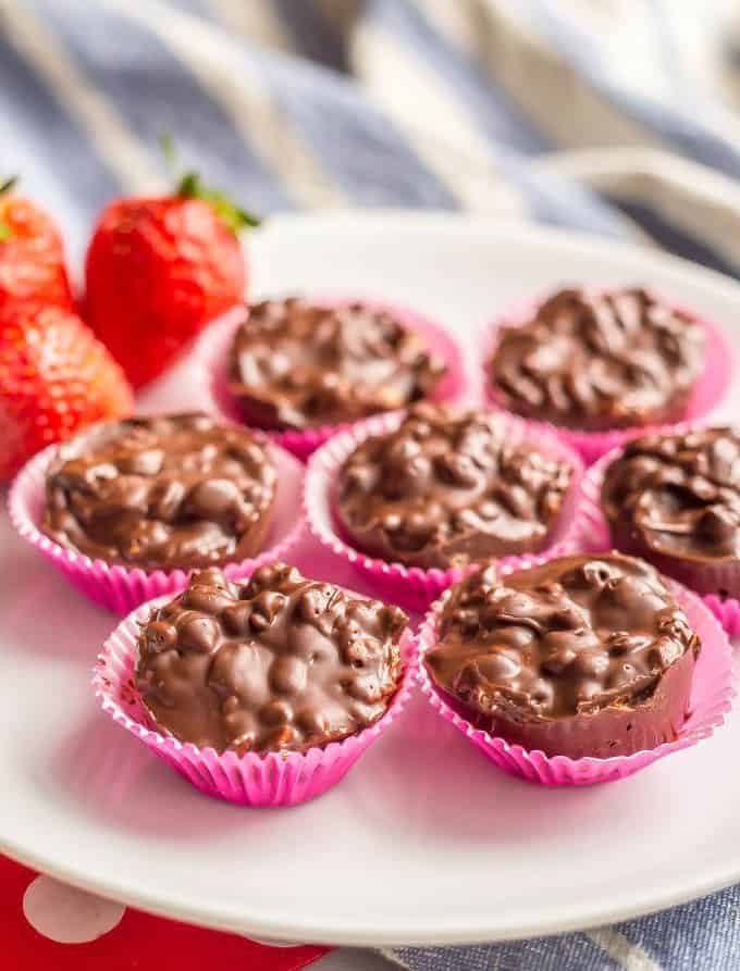 3-ingredient homemade crunch cups in pink wrappers on a white plate with strawberries and a blue striped towel underneath