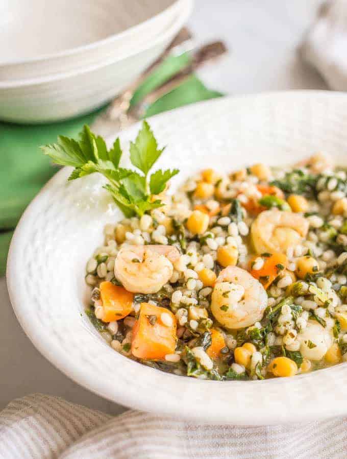Close-up side angle of lemon herb shrimp and veggies with barley with white bowls in the background