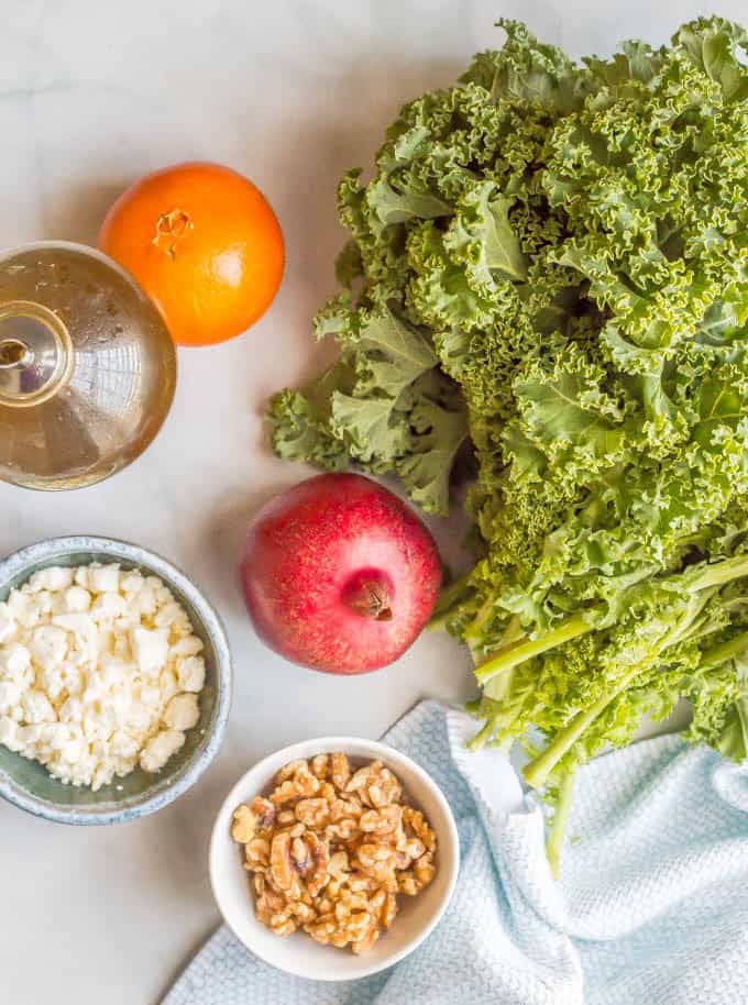 Winter kale salad with pomegranates ingredients laid out on a marble slab with a blue towel nearby