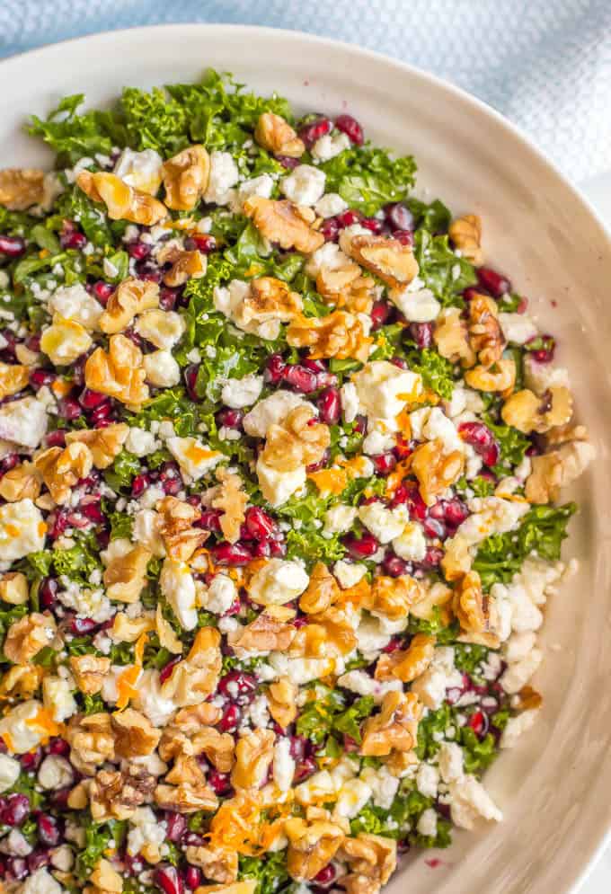 A winter salad with kale, walnuts, pomegranates and feta cheese served in a large white bowl.