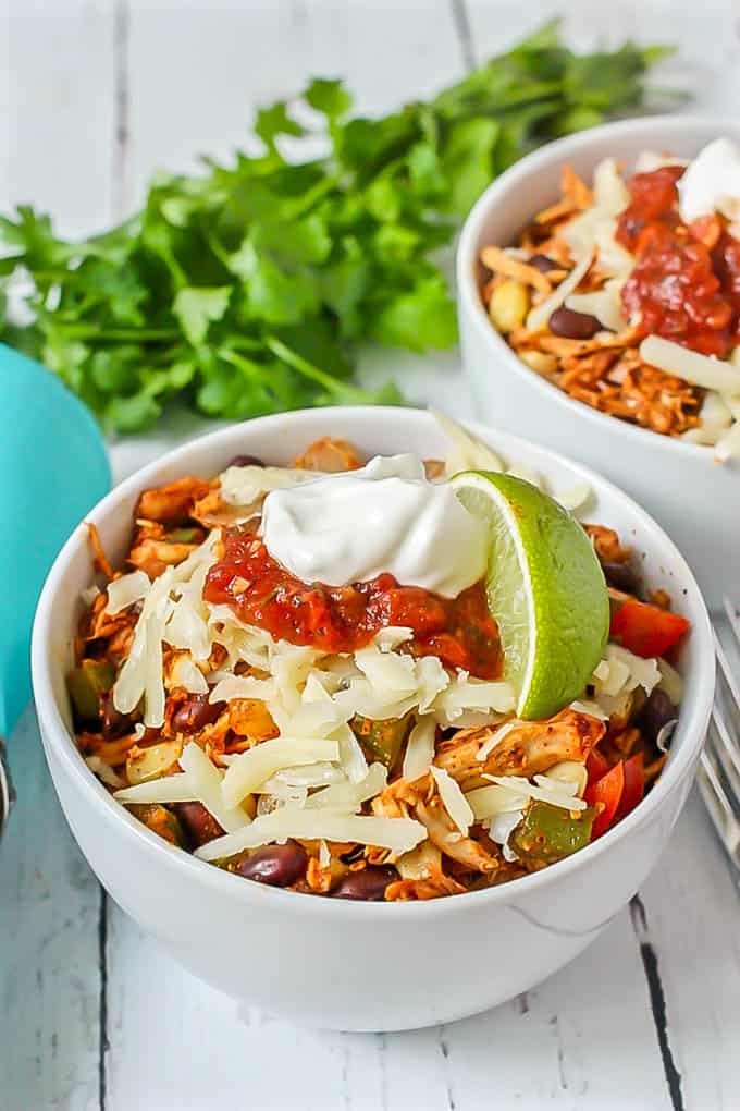 Southwest chicken skillet dinner being served in a white bowl with shredded cheese, salsa, Greek yogurt and a lime wedge on top