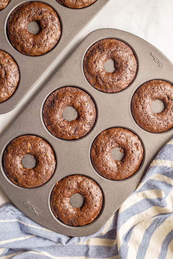 Overhead shot of whole wheat chocolate baked donuts in pan with a blue striped towel underneath