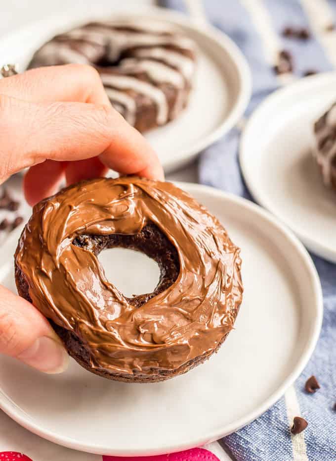 Whole wheat chocolate baked donut with Nutella glaze on a plate with scattered mini chocolate chips and a blue striped dish towel underneath