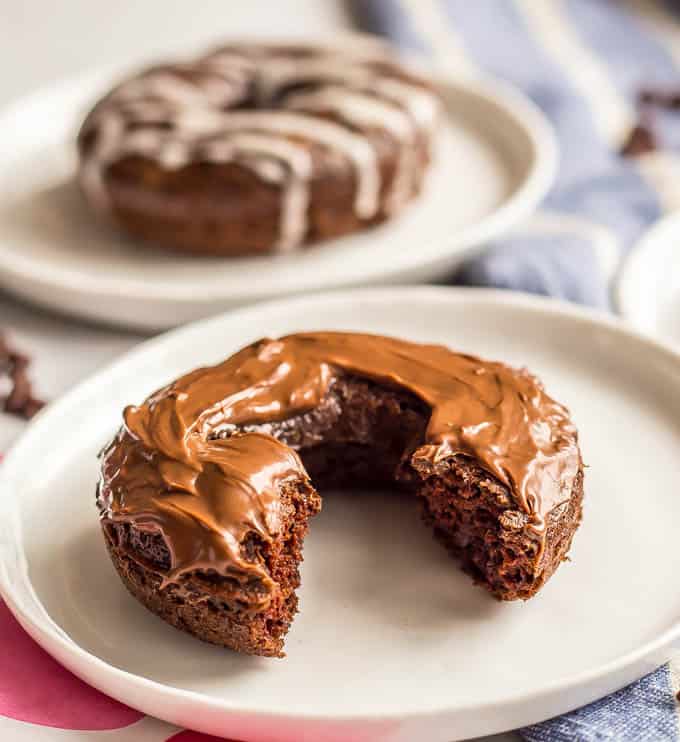 Whole wheat chocolate baked donut with Nutella frosting resting on a white plate with a bite taken out