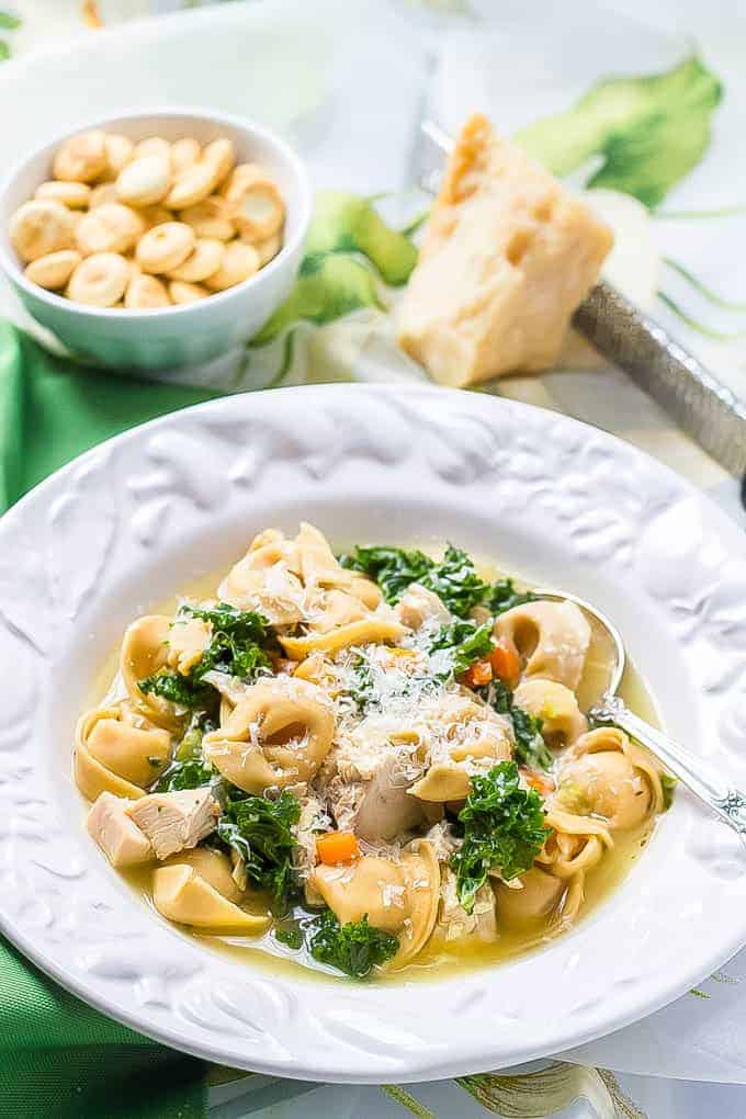 Chicken tortellini soup with kale being served in a white soup bowl with a spoon resting in the bowl