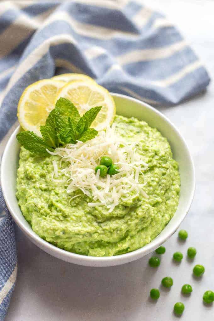 A bowl of healthy pea dip with Parmesan cheese sprinkled on top and a scattering of green peas nearby