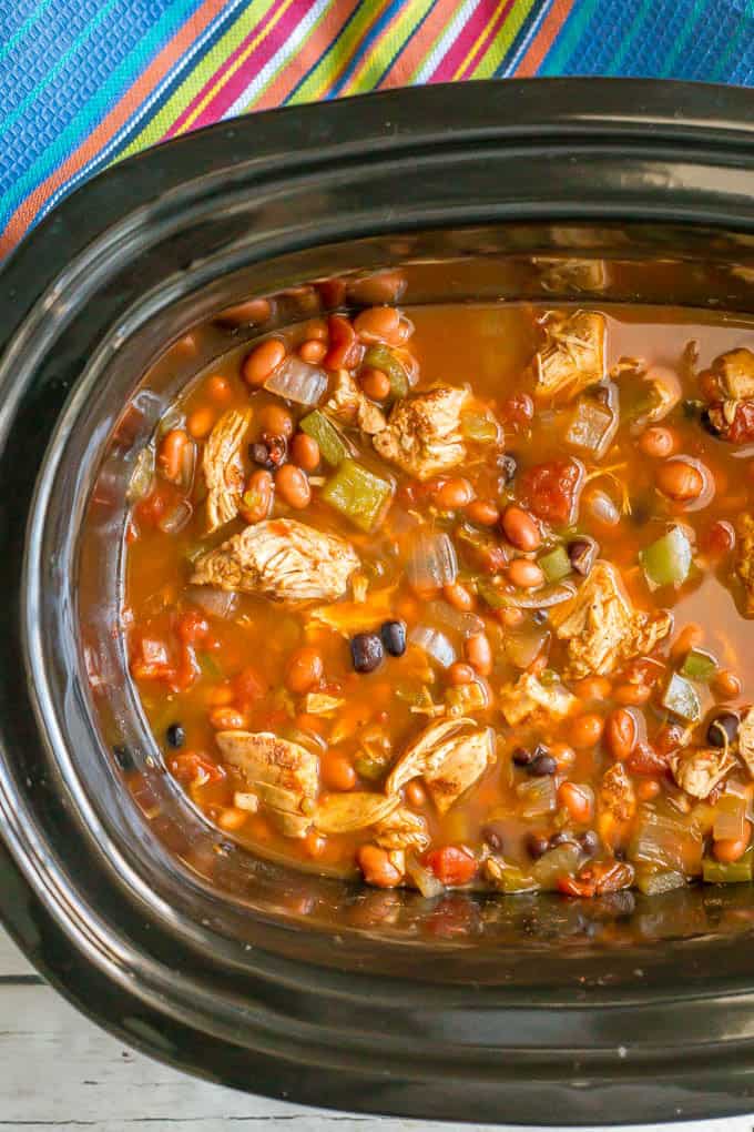 Healthy slow cooker chicken chili finished in the slow cooker with a colorful striped towel nearby