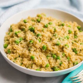 Close-up side angle of quinoa with peas and Parmesan in a large white bowl with a turquoise napkin and fork nearby