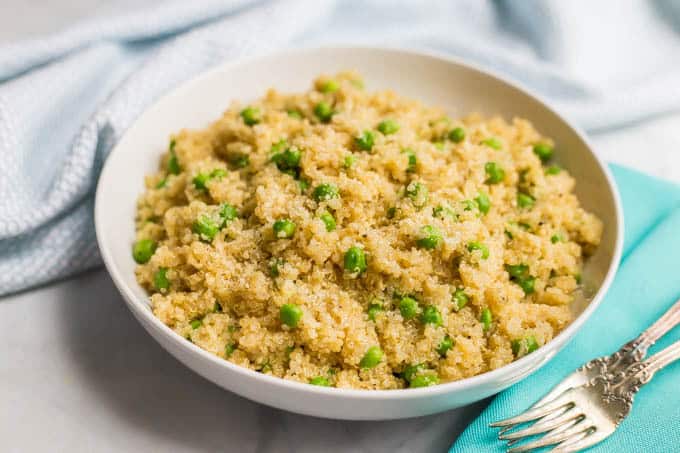 Close-up side angle of quinoa with peas and Parmesan in a large white bowl with a turquoise napkin and fork nearby