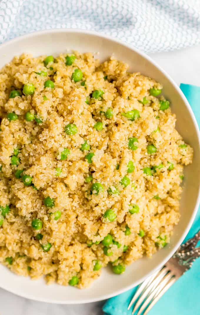 Close-up overhead angle of quinoa with peas and Parmesan in a large white bowl with a turquoise napkin and fork nearby