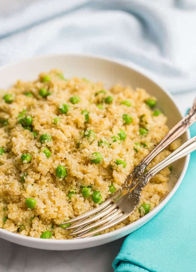 Close-up side angle of quinoa with peas and Parmesan in a large white bowl with a turquoise napkin nearby and two forks laid in the bowl