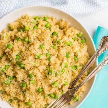 A bowl full of quinoa mixed with green peas and Parmesan and two forks resting in it.