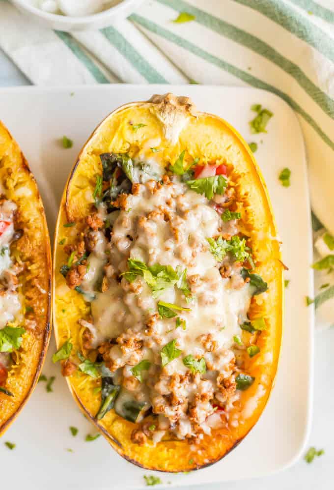 A close-up overhead shot of a turkey taco spaghetti squash boat with veggies and melted cheese being served on a large white plate