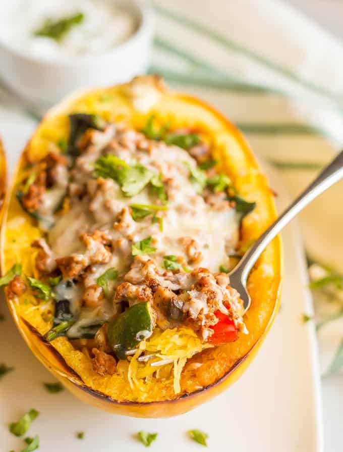 A forkful being taken out of a spaghetti squash boat stuffed with ground turkey taco meat and veggies