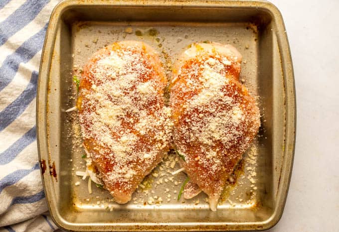 Two chicken breasts stuffed with prosciutto, spinach and mozzarella in a baking pan, topped with paprika and Parmesan cheese