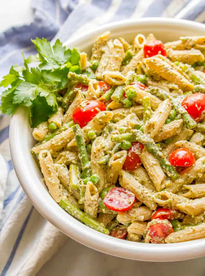 Side angle shot of creamy pesto pasta with spring vegetables and a garnish of parsley in a large white serving bowl